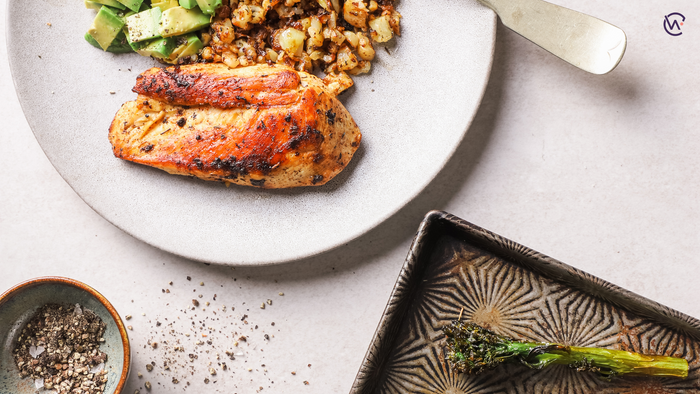 A plate of Chipotle chicken, garlic roasted cauliflower rice and avo next to a plate of a broccoli