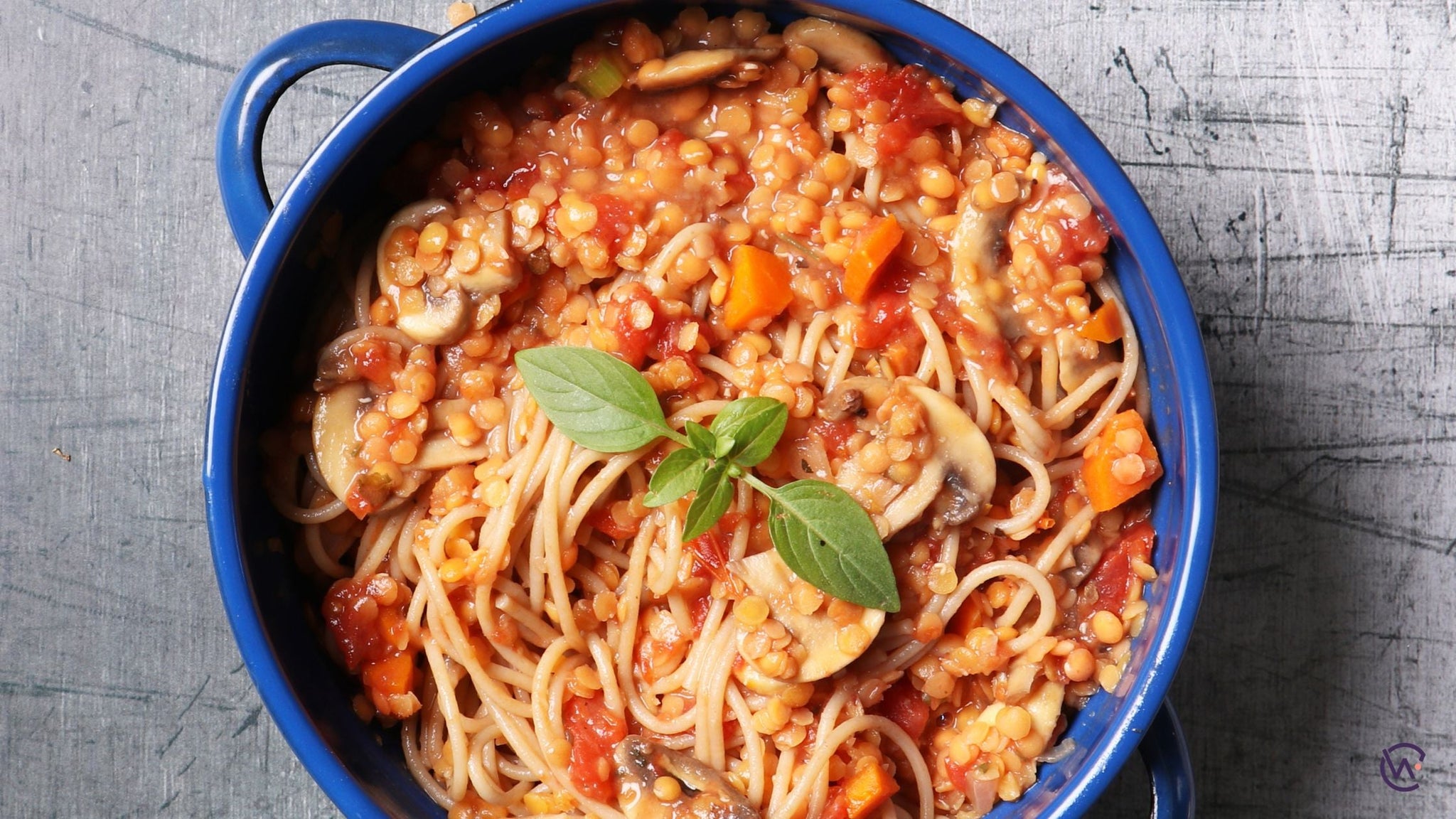 A blue bowl of lentil and mushroom bolognese with spaghetti